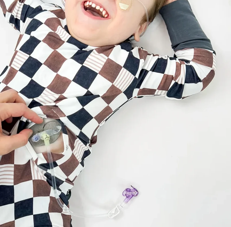 Girl wears black, brown and white checkered romper showing opening for feeding tube